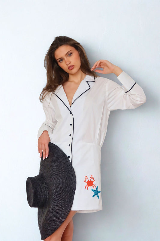 Woman wearing a white shirt dress with colorful designs on a light blue background